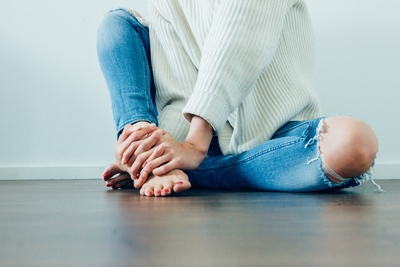 A woman in a thick woven sweater and ripped jeans sits cross-legged on a wooden floor